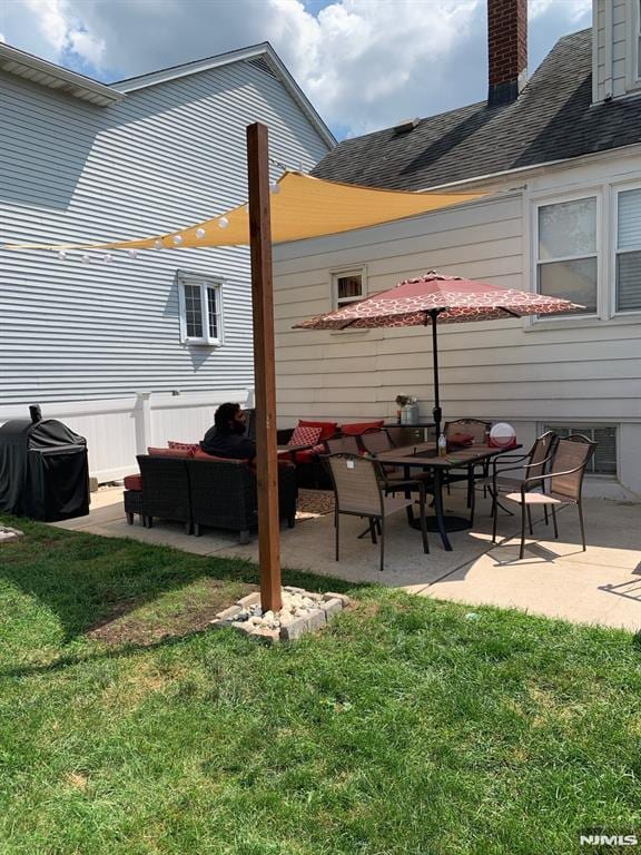 back of property with a chimney, a yard, roof with shingles, and a patio area