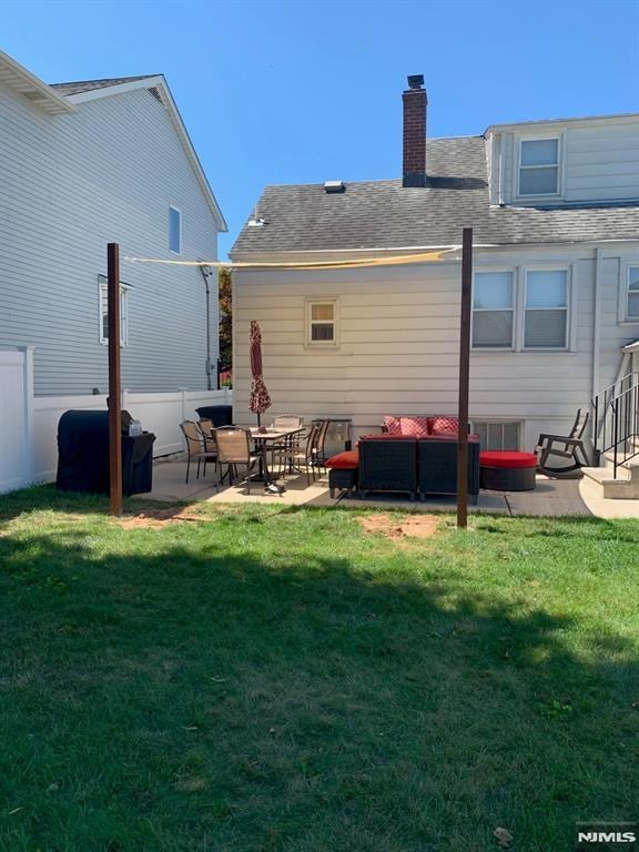 back of property with roof with shingles, a yard, a chimney, a patio, and fence