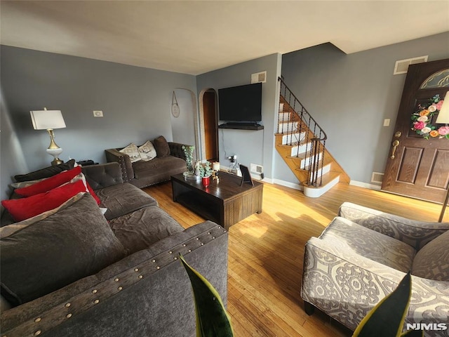 living room with wood-type flooring, visible vents, stairway, and baseboards