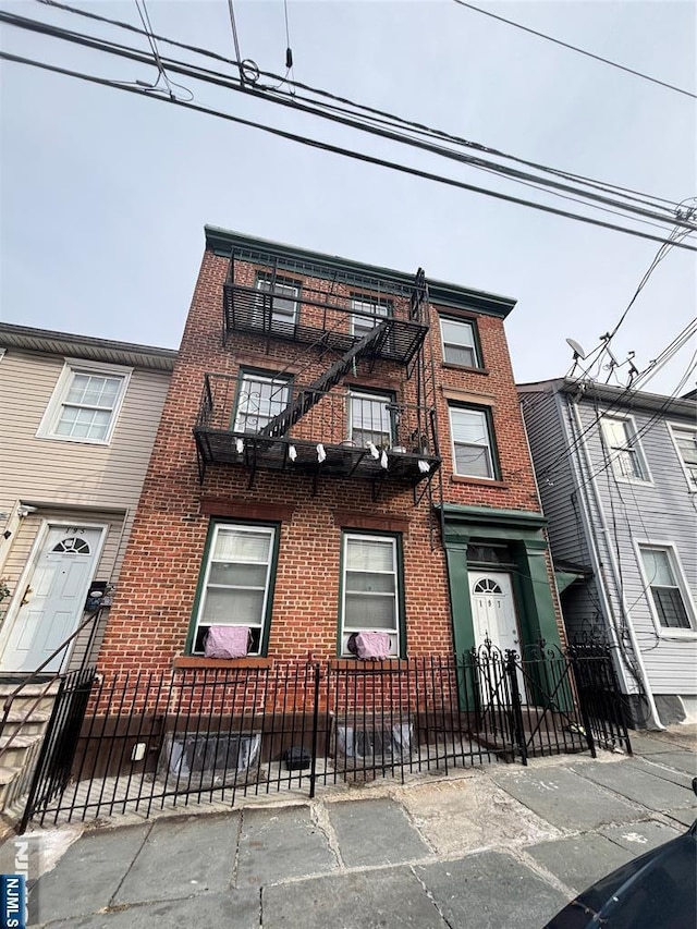 view of property featuring a fenced front yard, brick siding, and a balcony