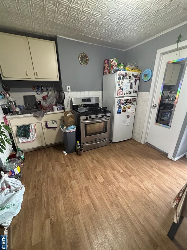 kitchen featuring stainless steel range with gas stovetop, light wood-style flooring, an ornate ceiling, and freestanding refrigerator