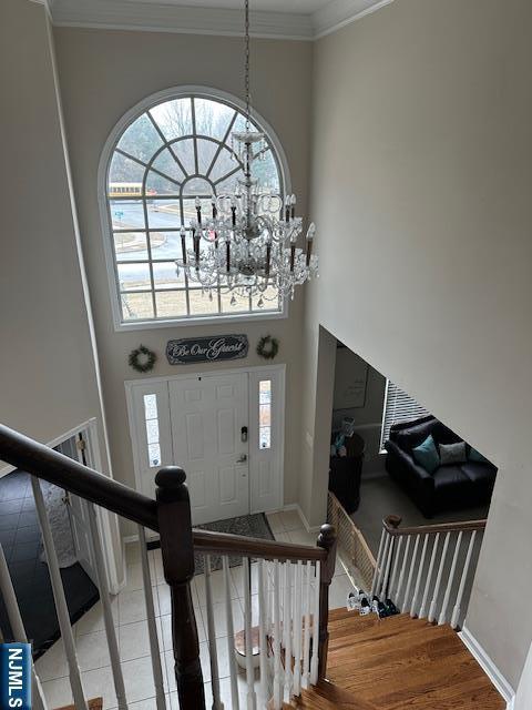 tiled entryway with a notable chandelier, a high ceiling, baseboards, stairway, and crown molding