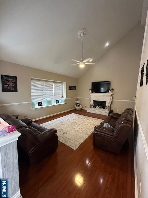 living room with vaulted ceiling, a ceiling fan, a fireplace with raised hearth, and wood finished floors