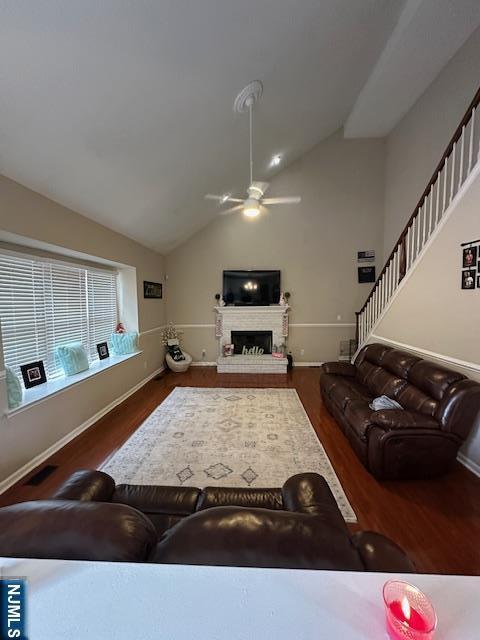 living room with a fireplace with raised hearth, wood finished floors, a ceiling fan, baseboards, and stairway