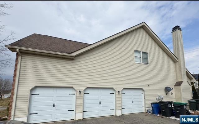 view of home's exterior with a garage, aphalt driveway, roof with shingles, and a chimney