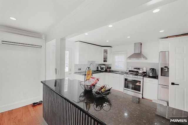 kitchen featuring tasteful backsplash, a wall unit AC, appliances with stainless steel finishes, wall chimney range hood, and white cabinetry