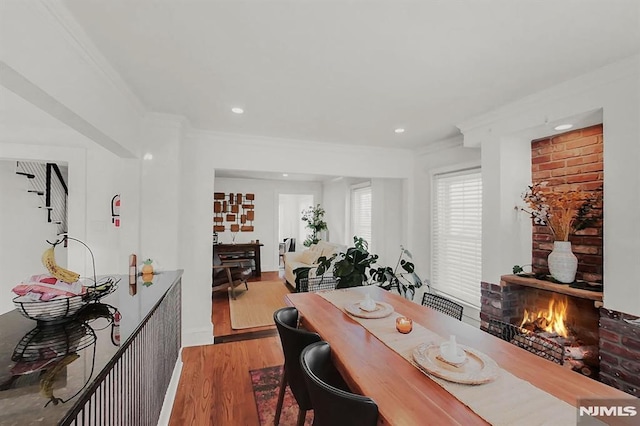 dining space featuring a brick fireplace, ornamental molding, wood finished floors, and recessed lighting