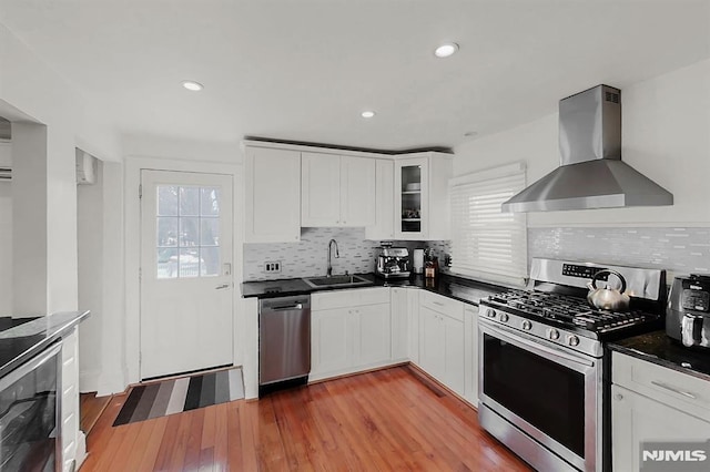 kitchen featuring light wood finished floors, wall chimney exhaust hood, wine cooler, stainless steel appliances, and a sink