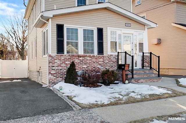 snow covered property entrance with aphalt driveway, brick siding, and fence