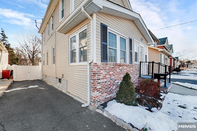 view of snow covered exterior featuring driveway, brick siding, and a gate