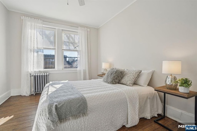 bedroom featuring lofted ceiling, wood finished floors, baseboards, radiator, and crown molding