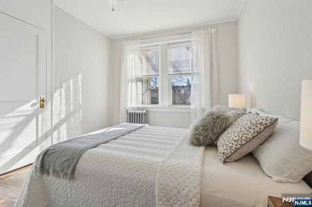 bedroom with ornamental molding, radiator, and wood finished floors