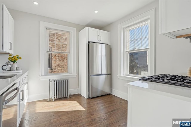 kitchen with dishwashing machine, white cabinets, freestanding refrigerator, radiator, and dark wood finished floors