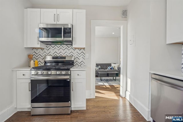 kitchen featuring dark wood-style flooring, light countertops, backsplash, appliances with stainless steel finishes, and white cabinetry