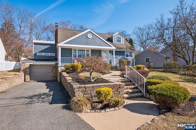 view of front of property with fence, a porch, driveway, stone siding, and an attached garage