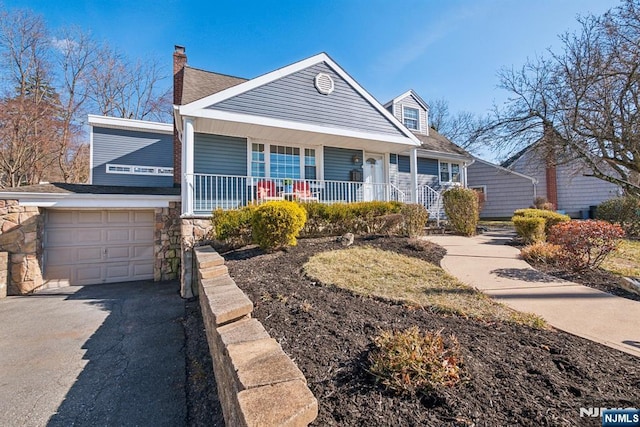 view of front facade featuring driveway, a porch, an attached garage, a chimney, and stone siding