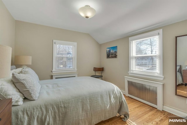 bedroom featuring radiator heating unit, multiple windows, vaulted ceiling, and wood finished floors