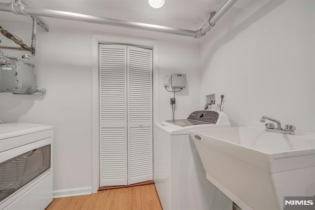 washroom featuring laundry area, a sink, light wood-style flooring, and washing machine and clothes dryer