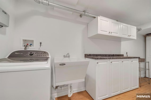 clothes washing area with a sink, washer / dryer, light wood-style floors, and cabinet space