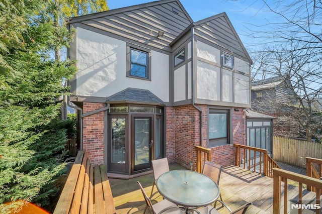 back of house featuring brick siding, fence, a deck, and stucco siding