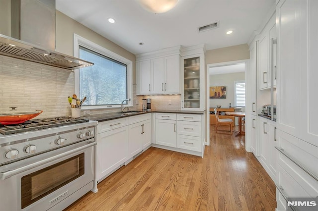 kitchen with visible vents, white cabinetry, a sink, wall chimney range hood, and high end stove