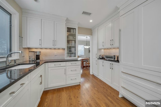 kitchen featuring light wood finished floors, visible vents, white cabinets, and a sink