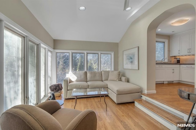 living room featuring lofted ceiling, light wood-style flooring, arched walkways, and recessed lighting