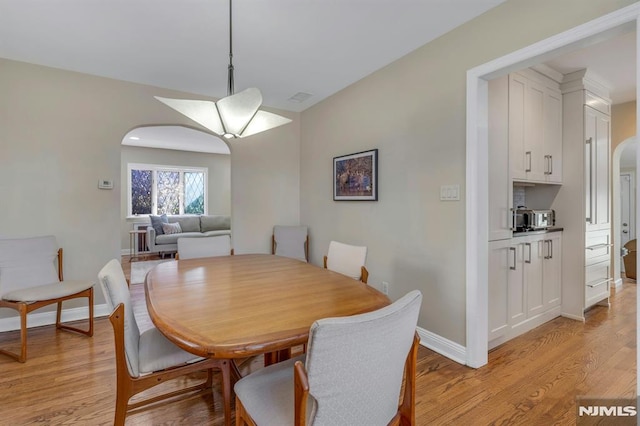 dining area featuring arched walkways, light wood finished floors, and baseboards