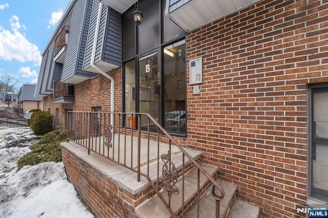 snow covered property entrance with brick siding