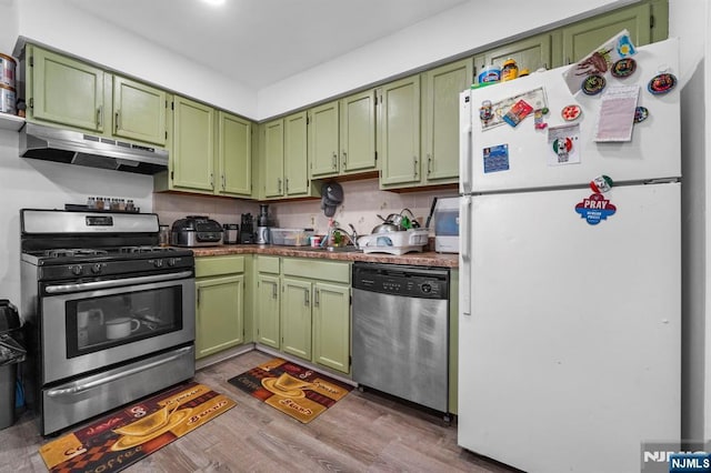 kitchen with under cabinet range hood, a sink, green cabinets, appliances with stainless steel finishes, and dark wood-style floors