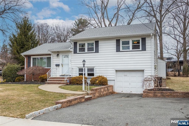 tri-level home featuring an attached garage, aphalt driveway, a front lawn, and roof with shingles