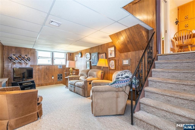 carpeted living room featuring a paneled ceiling, stairway, wood walls, and visible vents