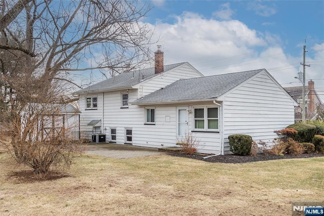 rear view of property featuring a lawn, a patio, a chimney, roof with shingles, and central air condition unit