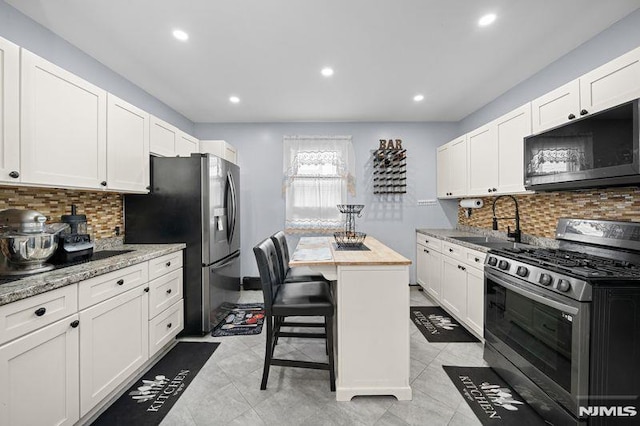 kitchen with light stone counters, a center island, appliances with stainless steel finishes, white cabinetry, and a sink