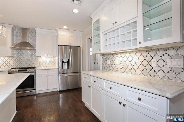 kitchen with dark wood finished floors, white cabinets, appliances with stainless steel finishes, light stone counters, and wall chimney range hood