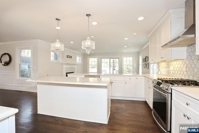 kitchen with a peninsula, a sink, light countertops, appliances with stainless steel finishes, and wall chimney range hood