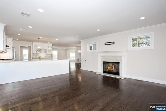 unfurnished living room with dark wood-style floors, a high end fireplace, visible vents, and crown molding