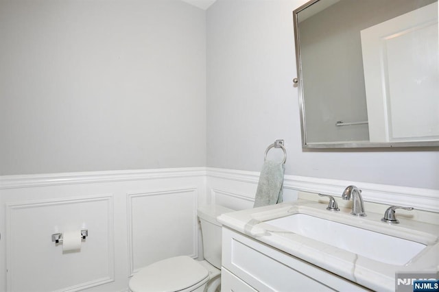 bathroom with toilet, a wainscoted wall, a decorative wall, and vanity