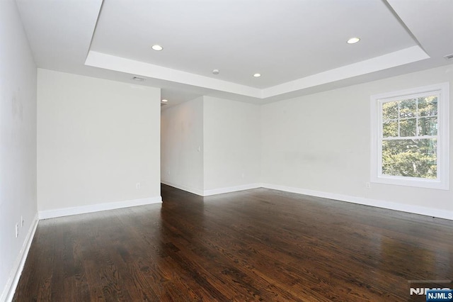 unfurnished room featuring dark wood-type flooring, recessed lighting, a raised ceiling, and baseboards