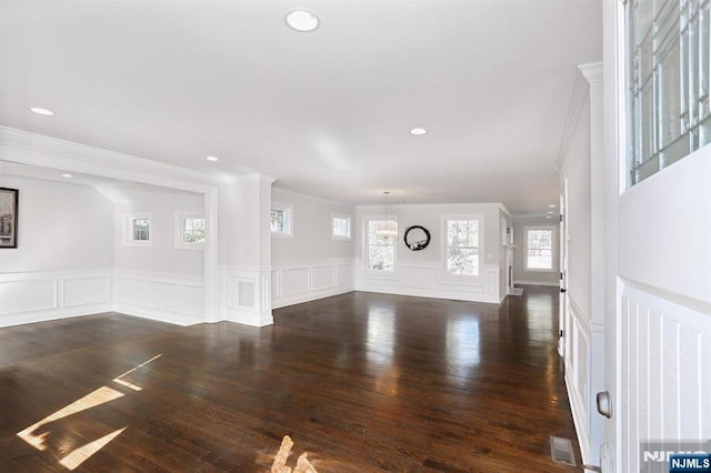 unfurnished living room featuring dark wood-style floors, a decorative wall, crown molding, and recessed lighting