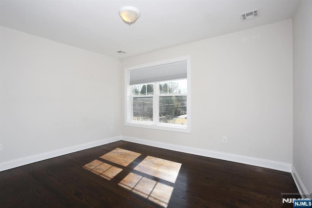 unfurnished room with dark wood-type flooring, visible vents, and baseboards