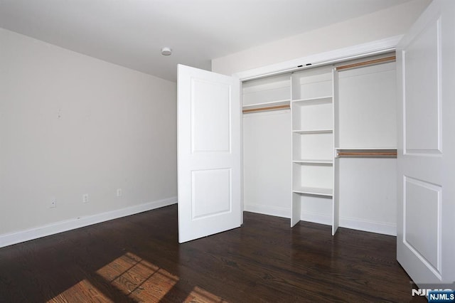 unfurnished bedroom featuring dark wood-type flooring, a closet, and baseboards