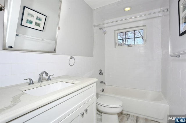 bathroom with tile walls, toilet, washtub / shower combination, vanity, and wood finished floors