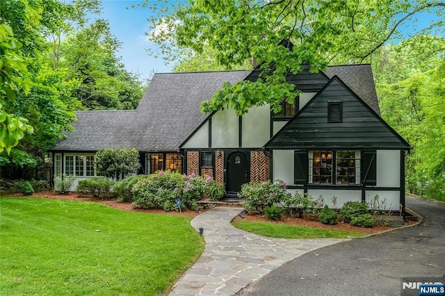 tudor home with stucco siding, a front lawn, and roof with shingles