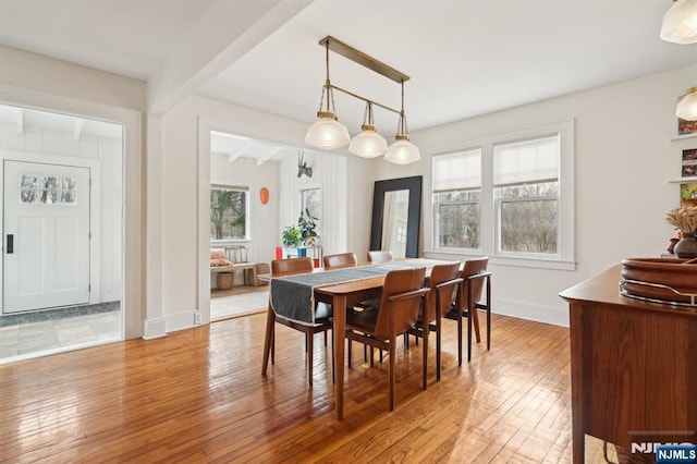 dining space with baseboards, beamed ceiling, and light wood-style floors