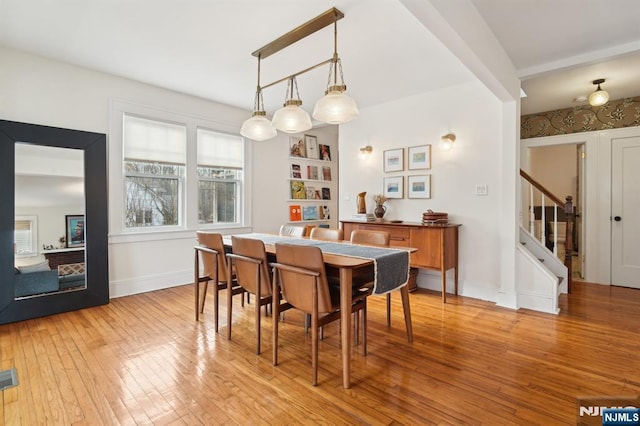 dining space with light wood-style floors, baseboards, and stairway