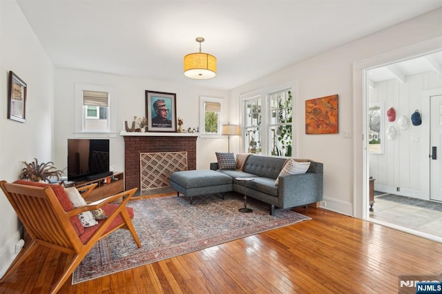 living area featuring a brick fireplace, hardwood / wood-style flooring, and baseboards