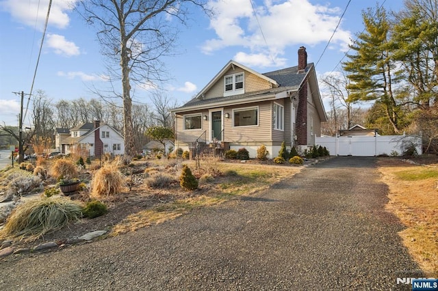 bungalow-style home with aphalt driveway, a chimney, and fence