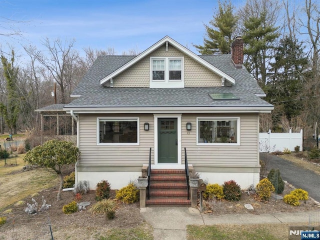 bungalow-style home with a chimney, fence, and roof with shingles