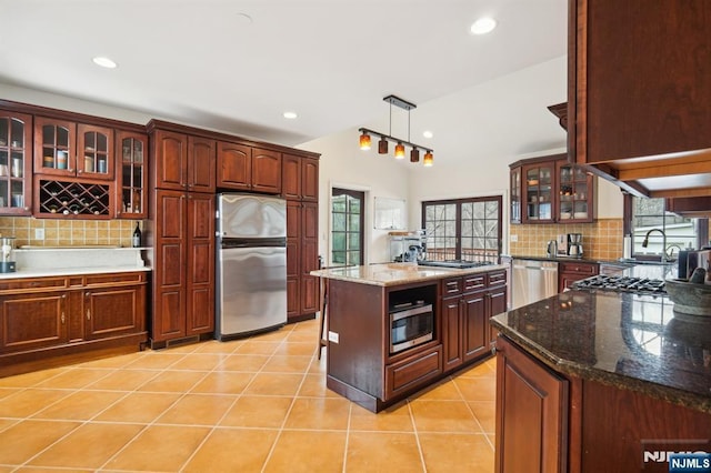 kitchen with glass insert cabinets, backsplash, stainless steel appliances, a sink, and light tile patterned flooring